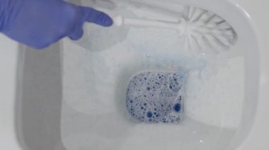 Wall mounted toilet cleaning with detergent. Woman hotel maid cleans a bathroom toilet with a scrub brush. household service. Modern flush toilet. Cleaning