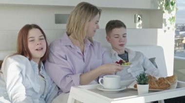 Mother having breakfast in bed with her childrens at mothers day. family breakfast in bedroom. Happy mother with her little daughter and son having breakfast together in bed at home.