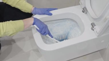 Wall mounted toilet cleaning with detergent. Woman hotel maid cleans a bathroom toilet with a scrub brush. household service. Modern flush toilet. Cleaning