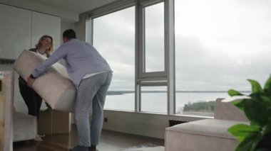 family rearranging furniture. Happy couple moving furniture in new apartment. Moving day, happy buyers. Positive smiling young couple moving furniture
