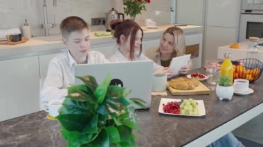 Young family with school kids have fun at breakfast time. Happy family eating healthy breakfast. Quality time with Family in kitchen eating together. Family Using Digital Devices At Breakfast