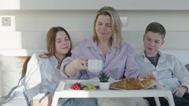 Mother having breakfast in bed with her childrens at mothers day. family breakfast in bedroom. Happy mother with her little daughter and son having breakfast together in bed at home.