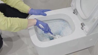 Wall mounted toilet cleaning with detergent. Woman hotel maid cleans a bathroom toilet with a scrub brush. household service. Modern flush toilet. Cleaning