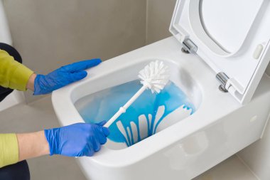 Wall mounted toilet cleaning with detergent. Woman hotel maid cleans a bathroom toilet with a scrub brush. household service. Modern flush toilet. Cleaning