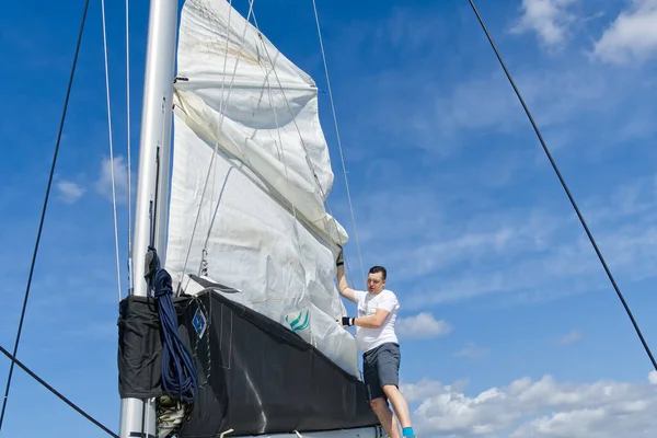 Raising the sail on a yacht. Young man captan lifting the sail of catamaran yacht during cruising. luxury sailing yacht, with sails being raised by rigging