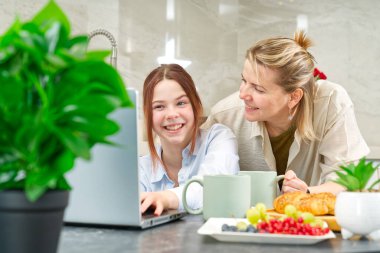 Happy mother and daughter having breakfast in kitchen and using digital devices. Lifestyle, Morning breakfast, mother and daughter together.