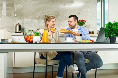 Young beautiful caucasian couple sitting at table while having breakfast at home Happy couple having breakfast together before leaving to work