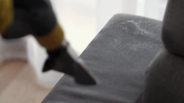 Kuru temizlemeci çalışanı mobilyalardaki toprağı temizliyor, yakın plan, elektrikli süpürge ile profesyonel ekipmanla temizliyor. Kanepeyi yıkama temizliği ile kapatıyoruz..