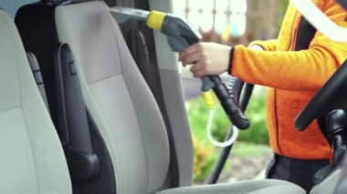 Tamirci arabanın ön tekstil koltuğunu elektrikli süpürgeyle süpürüyor. Adam temizleme işi Minivan.