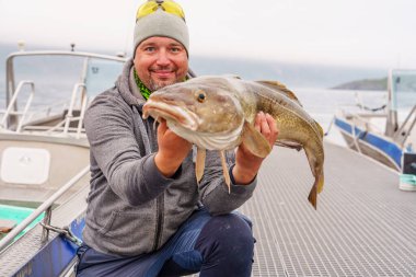 Fisherman with big cod fish. A Norwegian fisherman has caught a large Cod fish in Norwegian Fjord islands