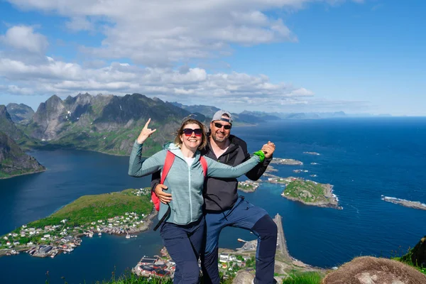 Happy Hiking couple enjoying Norway fjord view. Happy couple relax on top of Reinebringen, fjord. Active summer vacations Lofoten islands.