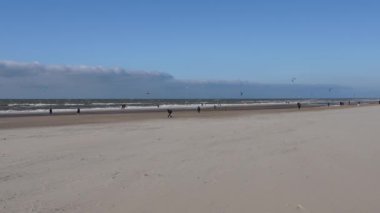 people walk and spend their free time on the beach in windy weather. The Netherlands. The beach with sea foam on a windy day. The Hague beach