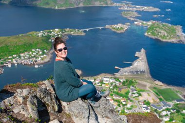 Happy woman hiker enjoys the panorama of lofoten islands at the top of Reinebringen. traveler alone on cliff edge in Norway lifestyle exploring concept. Hike above Reine village in the Lofoten