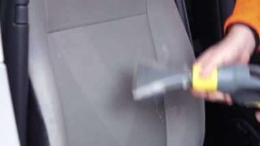 Tamirci arabanın ön tekstil koltuğunu elektrikli süpürgeyle süpürüyor. Adam temizleme işi Minivan.