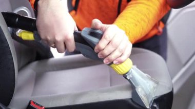 Tamirci arabanın ön tekstil koltuğunu elektrikli süpürgeyle süpürüyor. Adam temizleme işi Minivan.