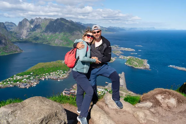 Happy Hiking couple enjoying Norway fjord view. Happy couple relax on top of Reinebringen, fjord. Active summer vacations Lofoten islands.