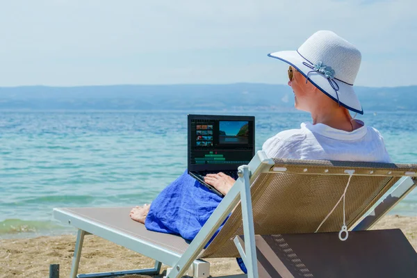 Video blogger, freelancer editing video at beach. Editing Videos On Laptop Using Video Editor App. Young woman working abroad on laptop while sitting on the beach, video editing freelance working