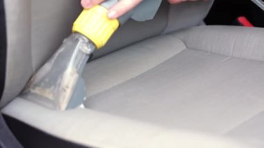 Tamirci arabanın ön tekstil koltuğunu elektrikli süpürgeyle süpürüyor. Adam temizleme işi Minivan.