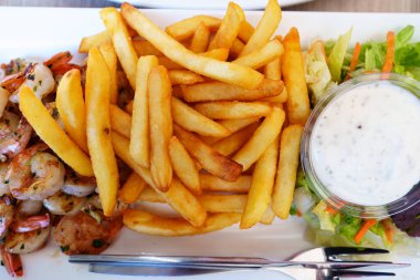 Lezzetli patates kızartması, kızarmış altın karides ve saf beyaz bir tabağa yerleştirilmiş lezzetli sarımsak sosu seyirciyi cezbedici sunumuyla cezbediyor..