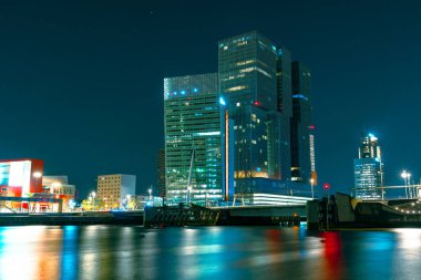 Rotterdam 'ın yüksek katlı mimarisinin göz kamaştırıcı gece manzarası yıldızlı gece gökyüzünün zeminine karşı dik duruyor, muhteşem ve büyüleyici bir şehir manzarası yaratıyor..