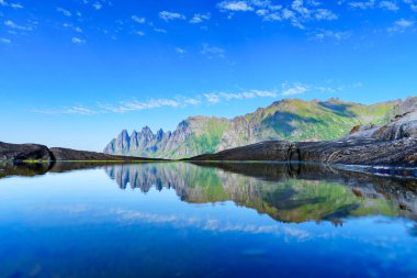 Norveçli bir yaz gününün nefes kesici bir görüntüsü, dingin denizi, görkemli dağları ve gökyüzündeki çarpıcı yansımaları ile peri masalı manzarasını yakalıyor..