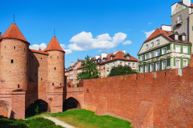 This image showcases a medieval city wall featuring two tall towers against a clear blue sky. The red brick structure has a crenellated top, surrounded by trees and distant buildings. clipart