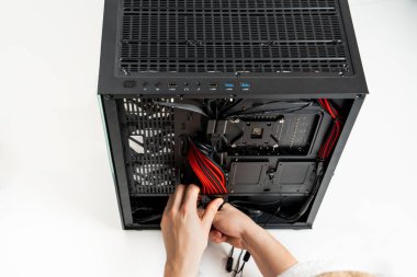 Odaklanmış bir birey, parlak siyah bir bilgisayar çantasına çeşitli donanım parçaları yerleştirirken görülüyor. Dosya açık, içeriyi ortaya çıkarıyor, bu arada kişinin elleri bileşenleri ayarlarken...