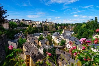 Lüksemburg. Resim, içinden sakin bir nehrin aktığı antik bir Avrupa şehrinin güzel bir manzarasını sergiliyor. Yemyeşil tepeler, tarihi ve büyüleyici bir karışımın vurgulandığı sahneyi oluşturur.