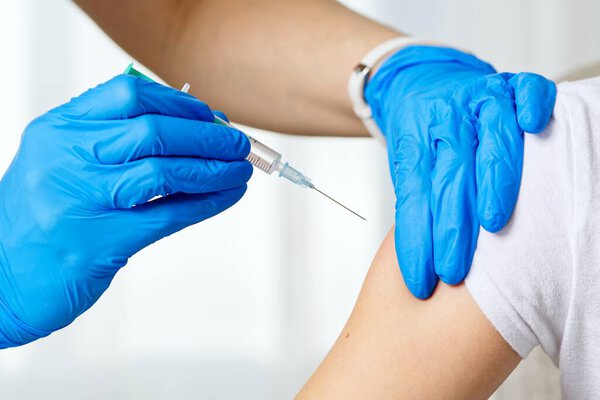 A healthcare professional in blue gloves administers a vaccine to a patient wearing a white T-shirt. The scene emphasizes the importance of vaccinations in promoting public health and wellness.