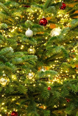 Kırmızı, altın ve beyaz ışıklarla süslenmiş güzel dekore edilmiş bir Noel ağacının yakın çekimi. Ağaç süslerle ve ışıklarla dolu. Sıcak ve şenlikli bir atmosfer yaratıyor..