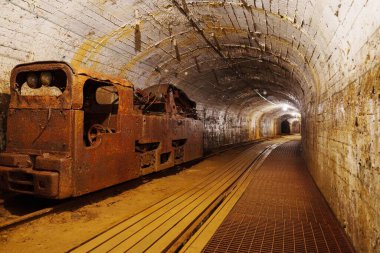 Paslı eski bir maden treni karanlık bir tünelde terk edilmiş olarak duruyor. İzler gölgelere gidiyor, gizemli bir atmosfer yaratıyor, madencilik ve endüstri ile ilgili hikayeler için ideal..