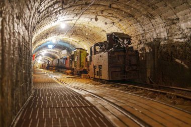 Paslı eski bir maden treni karanlık, ürkütücü bir maden tünelinde duruyor. Ahşap izler tozla kaplı ve atmosfer gergin. Terk edilme ve gizem hissi uyandırıyor..