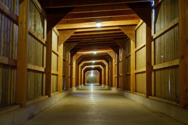 Bu geniş ahır koridorunda yüksek tavanı, kırsal ahşap duvarları ve dayanıklı beton zemini olan uzun bir yerleşim yeri var. Tavandan sarkan zarif ışıklar sıcak bir ortam yaratıyor..