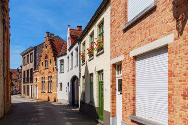Brugge, Belçika 'da eski tuğla evlerle dolu dar bir sokak. Çakıl taşı caddesinde ağaçlar ve saksılar var. Tarihi şehir merkezinin cazibesini sergiliyorlar..
