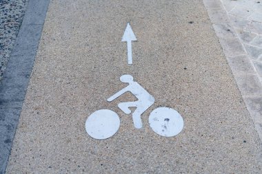 Fotoğraf beton yol yüzeyinde beyaz boyalı bisiklet yolu tabelasını gösteriyor. İşaret açık ve anlaşılması kolay. Bu da şeridin bisikletçilere tahsis edildiğini gösteriyor..