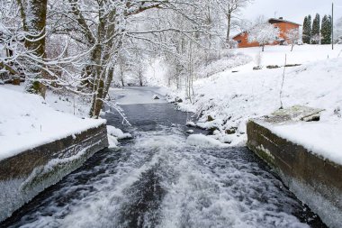 The image depicts a stunning winter landscape featuring a river winding through snow-covered banks and trees, evoking a serene atmosphere ideal for relaxation and winter adventures. clipart