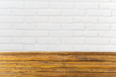 Bu resim, yumuşak bulanık beyaz tuğla bir duvara dayanan ve yaratıcı projeler, sunumlar ve fotoğrafçılık için ideal hale getiren, sıcak dokusu olan, kırsal ahşap bir masa kaplamasını içeriyor..