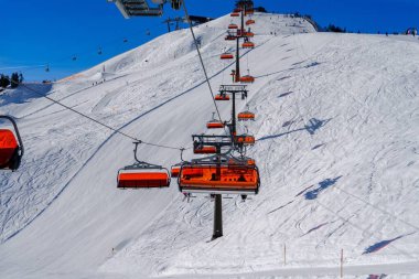 Sandalye, Avusturya 'nın Alplerdeki bir kayak merkezinde kayakçıları ve snowboardcuları dağın tepesine taşıyor. Kayakçılar ve snowboardcular güzel manzaranın ve temiz havanın tadını çıkarıyorlar..