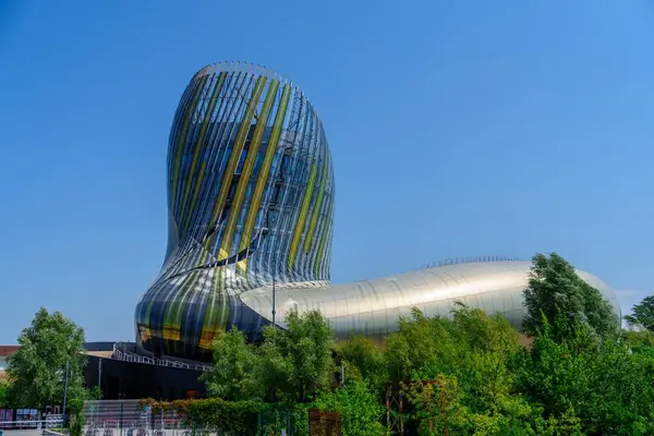 Canlı yeşil ağaçlarla çevrili, yansıtıcı panelleri ve çarpıcı mimarisi olan modern bir metalik müze, parlak mavi gökyüzüne karşı kurulmuş, çarpıcı bir görsel deneyim yaratıyor..