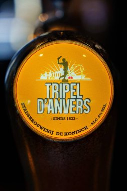 Antwerp, Belçika, 21.04.2025 Tripel Danvers. Bu yakın plan, Belçika 'nın zengin bira üretimini yansıtan bir içeceği gösteren altın etiketli ve yerel bira amblemiyle süslenmiş bir bira musluğunu vurguluyor.