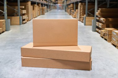 Bir depoda bir yığın karton kutu bekliyor. Bu sahnede lojistik ve malların taşınması vurgulanıyor. Teslimat ve nakliye hazırlıkları gözler önüne seriliyor..