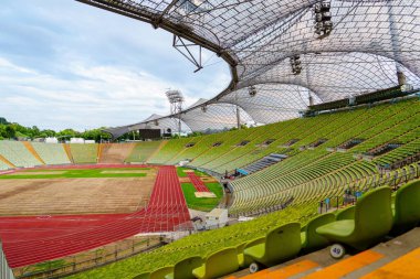 Yeşil katmanlı bir stadyum tribününün çarpıcı manzarası ve parlak kırmızı koşu pisti, eşsiz mimari sergileniyor, spor etkinlikleri ve mimari röfleler için mükemmel..