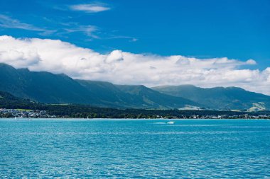 Sakin bir göl, parlak mavi bir gökyüzünün altında tüylü bulutlarla görkemli dağları yansıtır. Seyahat veya manzara fotoğrafçılığı için ideal, doğanın güzelliğini ve sükunetini vurgulamak.