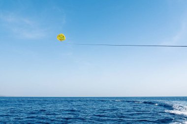 Canlı sarı bir paraşüt kuşu açık mavi denizin üzerinde süzülerek yaz eğlencesinin özünü yakalar. Seyahat promosyonları ve macera temalı projeler için idealdir..