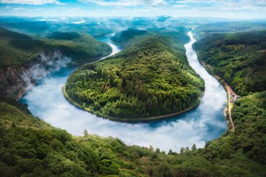 Yazın Mettlach (Orscholz, Saarland) yakınlarındaki Saarschleife 'yi göstermektedir. Saar nehri, yemyeşil ormanlarla çevrili çarpıcı bir at nalı kıvrımı yapar..