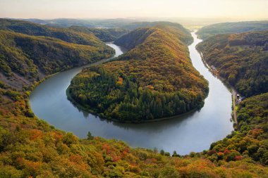 Görüntü sonbaharda Mettlach (Orscholz, Saarland) yakınlarındaki Saarschleife 'yi gösteriyor. Saar nehri, göz kamaştırıcı bir at nalı kıvrımında, canlı sonbahar renklerinde ormanlarla çevrili bir arazide süzülür..