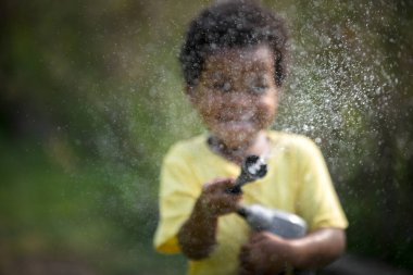 In the garden, a young African boy can be seen joyfully playing with a watering device.