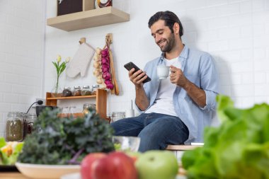 Mutfakta akıllı telefonu ve sebzesi olan genç bir adam.