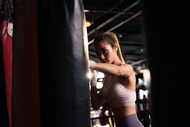 Spor salonunda yumruk torbasıyla boks yapan sağlıklı genç bir kadın..