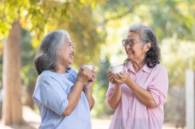 Park bahçesinde kahve fincanı olan Asyalı yaşlı çift emeklilik ve sağlıklı yaşam tarzı konsepti..